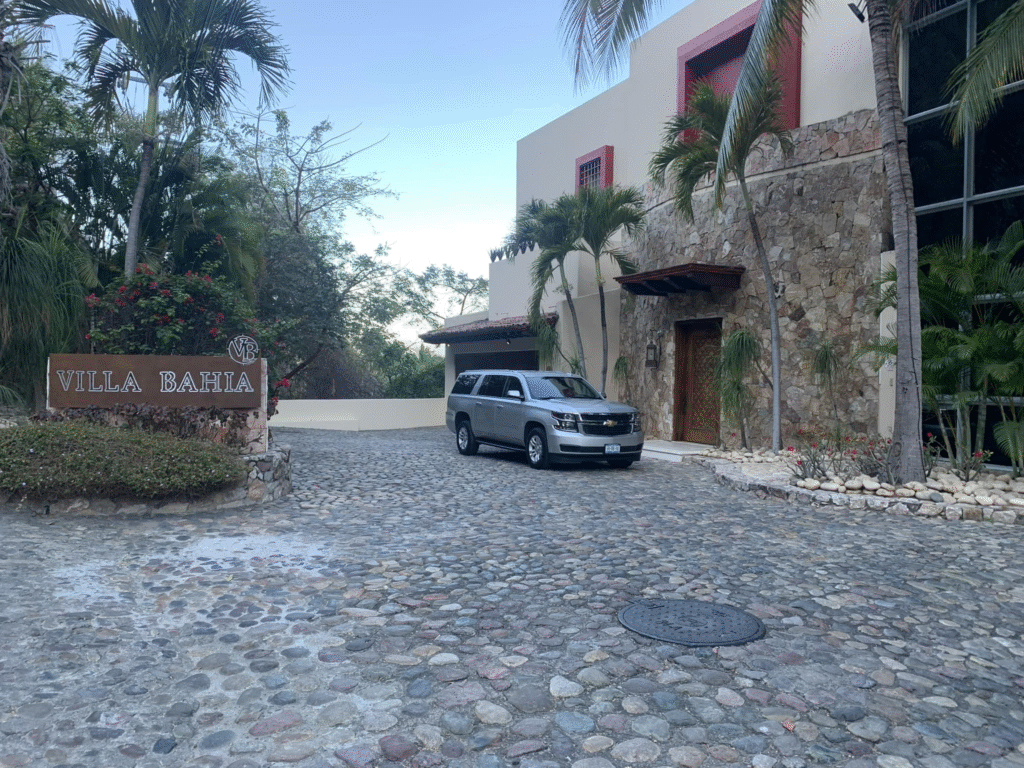SUV parked at the entrance of Villa Bahia with stone walls and tropical landscaping.